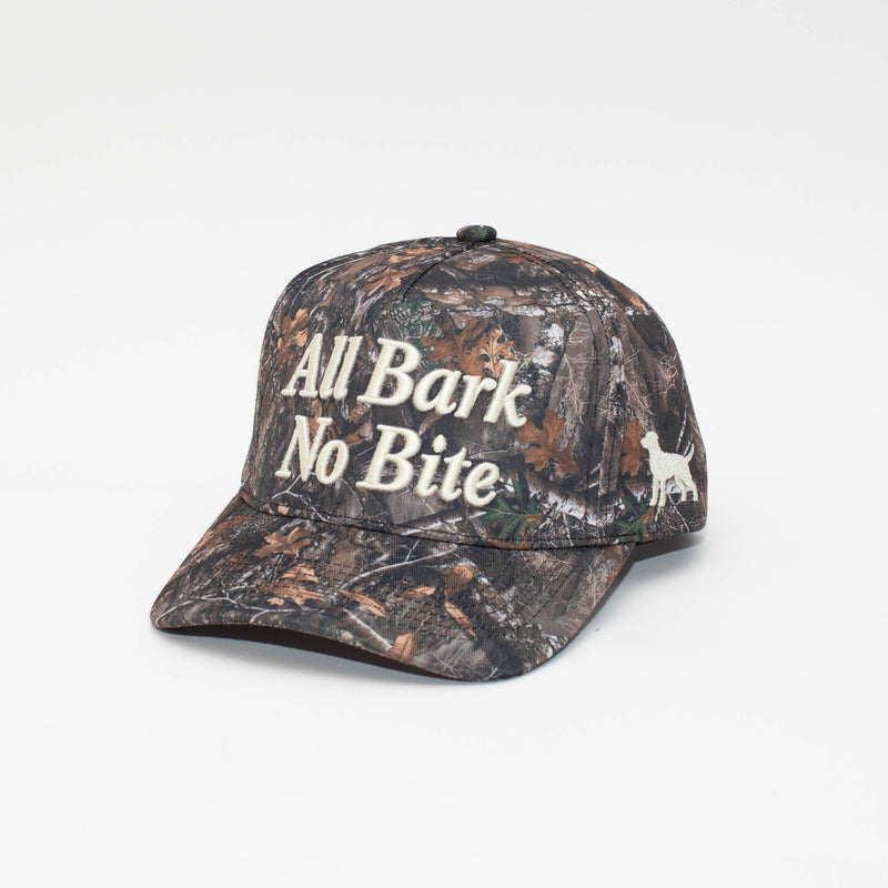 Angled view of the All Bark No Bite camo hat with cream embroidery and a dog silhouette on the side.